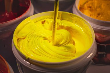 Beyaz bir kovada karıştırılan parlak sarı mürekkebi kapat, pürüzsüz, düzgün akışkanlığı ve zengin rengi ortaya çıkar, tekstil üzerine profesyonel ekran baskısı için hazırdır..