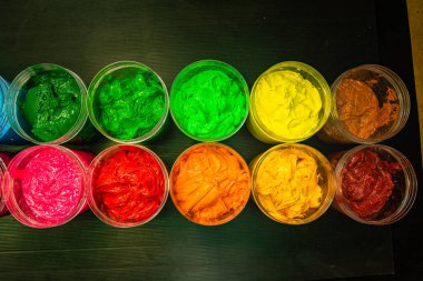 Her biri enerji ve yaratıcı potansiyelle patlayan kalın, canlı pigmentlerle dolu kusursuz bir daire şeklinde dizilmiş açık boya kavanozlarının büyüleyici yukarıdan aşağı görüntüsü..