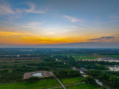 Barışçıl bir gündoğumu geniş kırsal alanları aydınlatarak, sel basmış pirinç tarlaları ve yeşil tarım arazileri boyunca sıcak altın ışığı yansıtıyor. Huzurlu sahne, kırsal kesimde sabahın erken saatlerinin sakin güzelliğini yakalar.