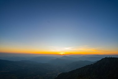 Katmanlı dağ sıralarının üzerinde nefes kesen bir gün batımı. Sıcak altın ışık, derin mavi gökyüzünde kayboluyor. Seyahat ve doğa temaları için ideal, dingin ve geniş bir doğal manzara yaratıyor..