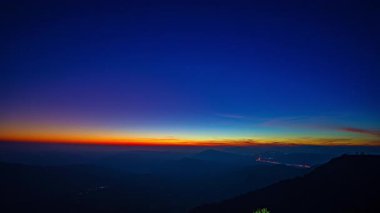 Güneş ışığı ormanlık tepelerin üzerine düşer, gökyüzünü turuncu ve mavinin hassas eğimleriyle boyarlar. Zaman atlaması, sakin bir dağ manzarasında sessizce uyanan doğayı yakalar..