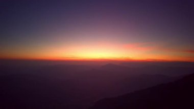 Parlak gün doğumu dağ ufkunu yavaşça aydınlatır, sıcak altın ışığın dokunduğu yuvarlanan sırtları ortaya çıkarır.