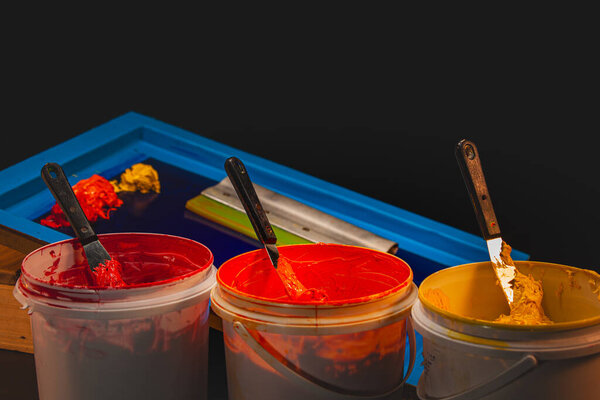 Hands spread warm toned inks across a screen frame, blending colors from soft yellow to intense red. Close up captures the texture, motion, and artistry involved in crafting vibrant gradient prints