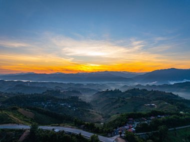 Sarmal bir asfalt yol, yemyeşil verimli tepeler boyunca uzanır, güzel bir gökyüzünün altında sabah sisiyle örtülü bir vadiye bakar. Bu manzaralı manzara özgürlüğün habercisidir.
