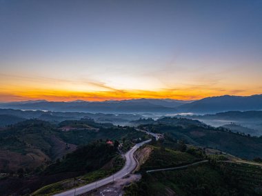 Panoramik Gün Doğumu Zaman Hızında Yakalandı. Yuvarlanan tepeler boyunca uzanan dolambaçlı bir asfalt yol. Bu manzara, doğanın barışçıl kırsal bir ortamda özgürlüğünü, seyahatini ve güzelliğini taşır..