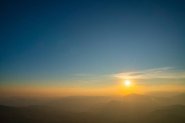 Yukarıdan izlenen sisli bir dağlık vadide sinematik gün doğumu. Parlayan ufuk, katmanlı dağlar ve sürüklenen sis doğa, meditasyon ve manzaralı seyahat kavramları için ideal rüya gibi bir ortam yaratır.