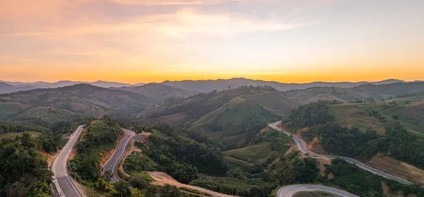 Tayland 'ın Nan Eyaleti' ndeki yüksek bir tepede, kıvrımlı bir dağ yolunda parlayan altın günbatımı ışığı çarpıcı bir kıvrım, zirveler ve sıcak akşam atmosferi manzarası yaratıyor..