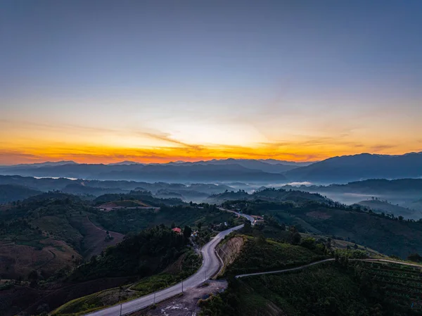 Panoramik Gün Doğumu Zaman Hızında Yakalandı. Yuvarlanan tepeler boyunca uzanan dolambaçlı bir asfalt yol. Bu manzara, doğanın barışçıl kırsal bir ortamda özgürlüğünü, seyahatini ve güzelliğini taşır..