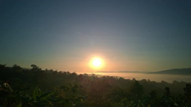İnsansız hava aracından görülen altın sabah ışığı, sis dolu dağlardan ve uçsuz bucaksız ufuklardan, dokunulmamış doğanın huzurlu ve manzaralı bir görüntüsünü sunuyor. Sisli Dağ Vadisi Sinema Uçağı Görünümü