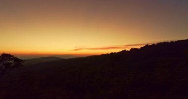 Sıcak bir günbatımı sisli dağların ve yüksek çam ağaçlarının katmanlarını aydınlatırken, ziyaretçiler de altın akşam ışığında manzaranın tadını çıkarıyorlar. Bu huzurlu manzara rahatlama ve seyahat çağrıştırıyor..