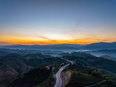 Panoramik Gün Doğumu Zaman Hızında Yakalandı. Yuvarlanan tepeler boyunca uzanan dolambaçlı bir asfalt yol. Bu manzara, doğanın barışçıl kırsal bir ortamda özgürlüğünü, seyahatini ve güzelliğini taşır..