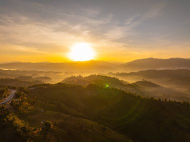 Nan Eyaleti 'ndeki yüksek dağ tepeleri boyunca kıvrılan, günbatımının yumuşak ışığıyla aydınlanan ve huzurlu doğal bir manzarayla çevrelenmiş dolambaçlı bir yolun havadan görünüşü..