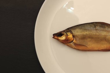 Siyah taş arka planda beyaz bir tabakta balık kafası çıkar..