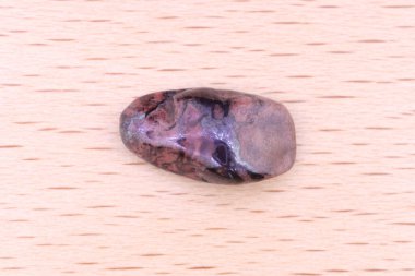 Hafif verniklenmiş ahşap zemin üzerinde sugilite mücevher taş dokusu. Makro yakın çekim.