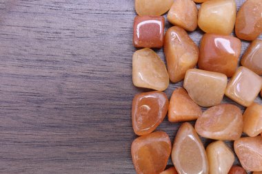 Kırmızı Aventurine hurda mücevheri, yarım kahverengi ahşap dokusunda. Yığın mineral çakıl taşı arka planı. Metin için yer.