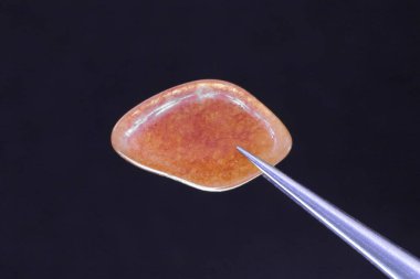 Kırmızı Aventurine mücevher deseni siyah arka planda cımbızla. Makro yakın çekim.