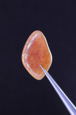 Kırmızı Aventurine mücevher deseni siyah arka planda cımbızla. Makro yakın çekim.