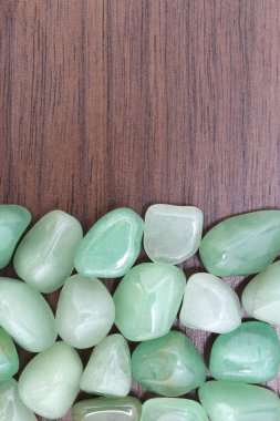 Yeşil Aventurine hurda mücevheri, yarım kahverengi ahşap dokusunda. Yığın mineral çakıl taşı arka planı. Metin için yer.