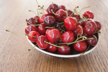 Kirazlar ahşap masada, su damlaları makro arka planda.