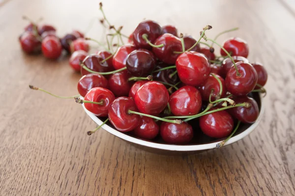 Kirazlar ahşap masada, su damlaları makro arka planda.