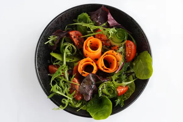 Bir kasede taze karışık sebze salatası. Beyaz arka planda siyah kasede çiğ salata.