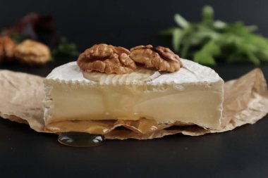 Camembert peyniri. Cevizli. Ağda kağıdında ve siyah arka planda.