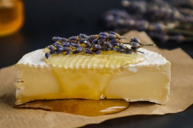 Camembert peyniri, lavantalı. Ağda kağıdının üzerinde ve siyah arkaplanda duruyor.