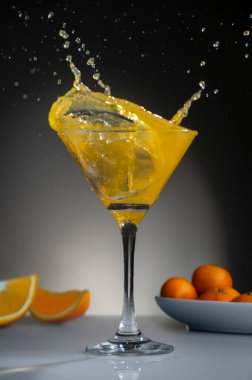 Portakal suyuyla kokteyl bardağı, bardaktan akan sıvı su ve dilimlenmiş portakallı bir tabak.