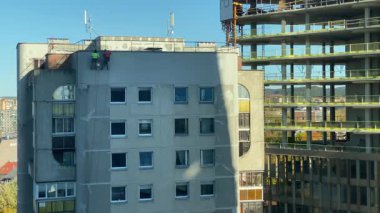 Çatıdan inen inşaat işçileri eski bir şehir binasının ön cephesini onarmak ve onarmak için emniyet kemerleri ve ipleri kullanıyorlar. Kentsel yenileme ve bakım süreci güneşli bir günde kaydedildi. Yüksek kalite 4K görüntü.