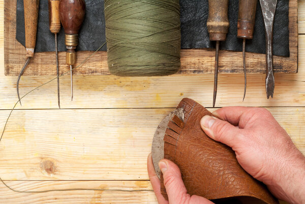 Leather craft tools on a wooden background. Craftmans working with leather using crafting DIY tools. Piece of hide and working  handmade tools on a work table. Copy space. Top view