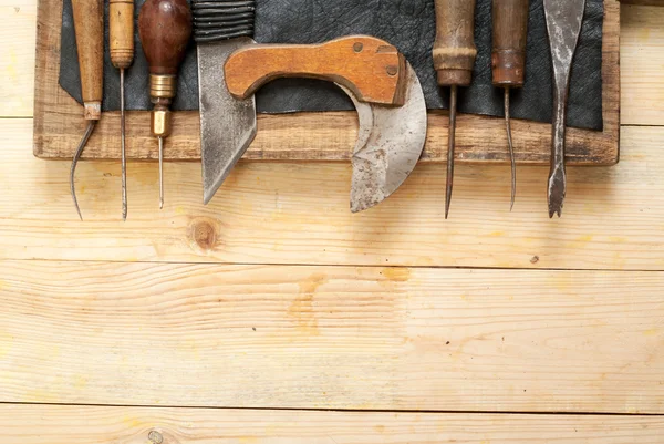 Kožené řemeslné nástroje na dřevěné pozadí. Craftmans pracovní stůl. Kus kůže a ručně vyráběných nástrojů. Pohled shora — Stock fotografie