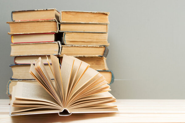 Open book, stack of hardback books on wooden table. Back to school. Copy space