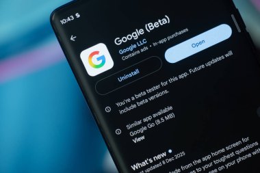 Dhaka, Bangladeş 26 Aralık 2025: Google Beta uygulama ekranını gösteren telefon, kulaklıklar mavi bir yüzey üzerinde dinleniyor