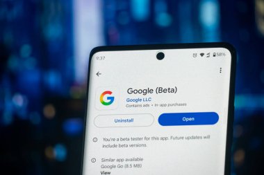 Dhaka, Bangladeş 26 Aralık 2025: Google Beta uygulama ekranını gösteren telefon, kulaklıklar mavi bir yüzey üzerinde dinleniyor