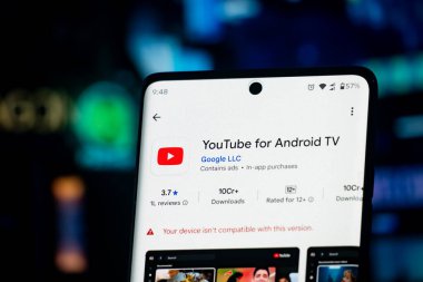 Dhaka, Bangladeş 'in 26 Aralık 2025: Android TV uygulama bilgileri için yakındaki kulaklıklar ile YouTube' u gösteren bir akıllı telefon ekranı