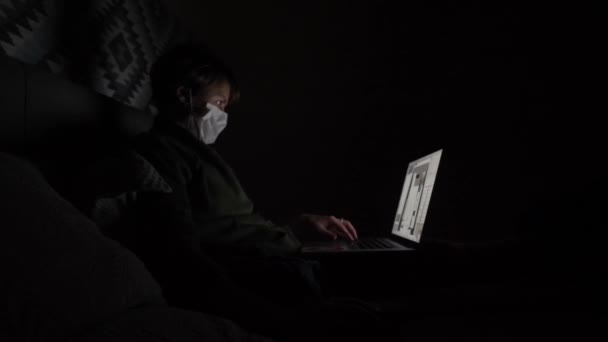 Dívka v lékařské masce pracuje ve tmě doma.. — Stock video
