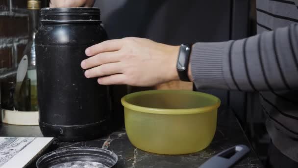 En man i köket tillsätter mjöl till en skål. — Stockvideo