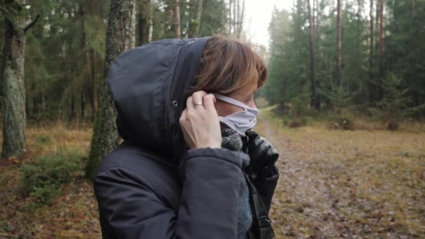 Una chica en ropa de abrigo se pone una máscara protectora en el bosque. — Vídeo de stock