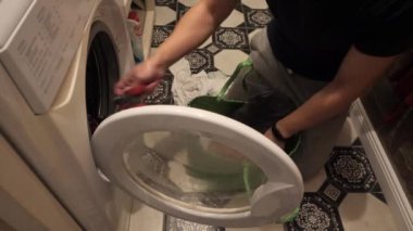 Bir adam kirli çamaşırları çamaşır makinesine koyar..