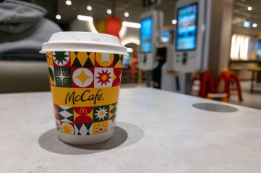 WARA, POLAND - 5 Ocak 2026 McDonalds restoranının masasında duran renkli bir McCafe kağıt kahve fincanı. Bulanık arkaplanda, dijital self-servis sipariş kioskları görünür