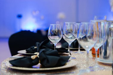 Kristal şarap kadehleri, siyah peçeteler ve altın tabaklar ile lüks şölen salonu veya düğün resepsiyonu için şık bir masa.