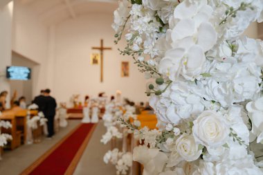 Güller ve orkidelerle süslenmiş zarif beyaz düğün süslemeleri kilise koridorunda romantik bir tören ortamı yaratıyor.