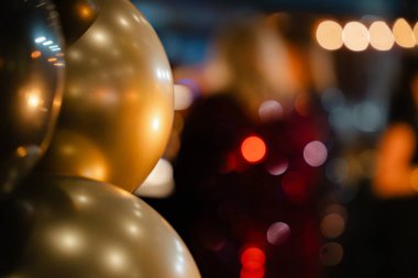 Yumuşak bokeh ışıkları olan şenlikli altın balonlar kutlama veya akşam etkinliği için sıcak ve zarif bir parti atmosferi yaratıyor.