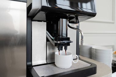 Profesyonel espresso kahve makinesi modern ofis mutfağında ya da büfe ortamında beyaz seramik fincana taze kahve dolduruyor.