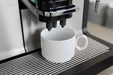 Profesyonel büfede ya da ofis mutfağında beyaz seramik bardağa sıcak içecek dağıtan modern kahve makinesi.