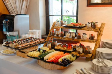 Pastalar, meyve tabakları ve cam kavanozlarla süslü zarif bir tatlı büfesi. Kırsal ahşap stantlar üzerine kurulmuş. İçi doğal ışık dolu samimi bir kafe.