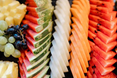 Renkli dilimlenmiş meyve tabağı ve karpuz karpuz üzümleri taze büfe sunumu için düzenli sırada dizilmiş ananas.