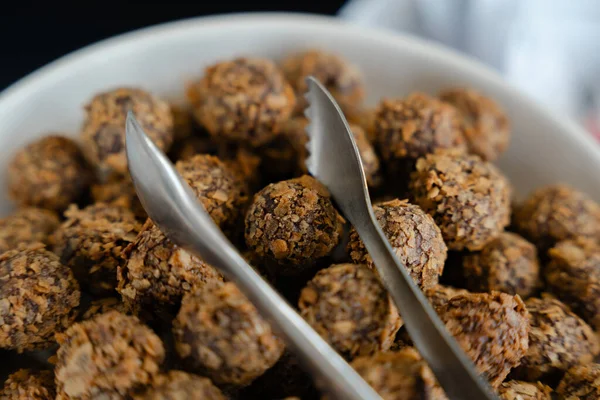 Tatlı büfesi için metal maşayla servis edilen kıtır kıtır çikolatalı enerji toplarıyla dolu zarif bir kase.