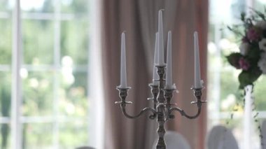 Zarif gümüş şamdanlarla süslenmemiş beyaz mumlar güzel dekore edilmiş bir masanın üzerinde duruyor. Parlak ve romantik bir ortamda, yumuşak doğal ışık büyük pencerelerden içeri akıyor.