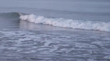 Okyanus dalgalarının yaklaşması kumlu bir sahilde ağır çekimde kırılıp yıkanması.